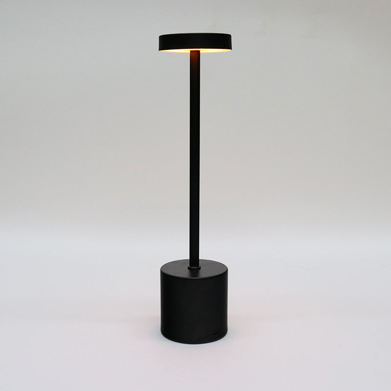 Black Skyscraper LED lamp lit, with warm light spilling from under the shade, on grey