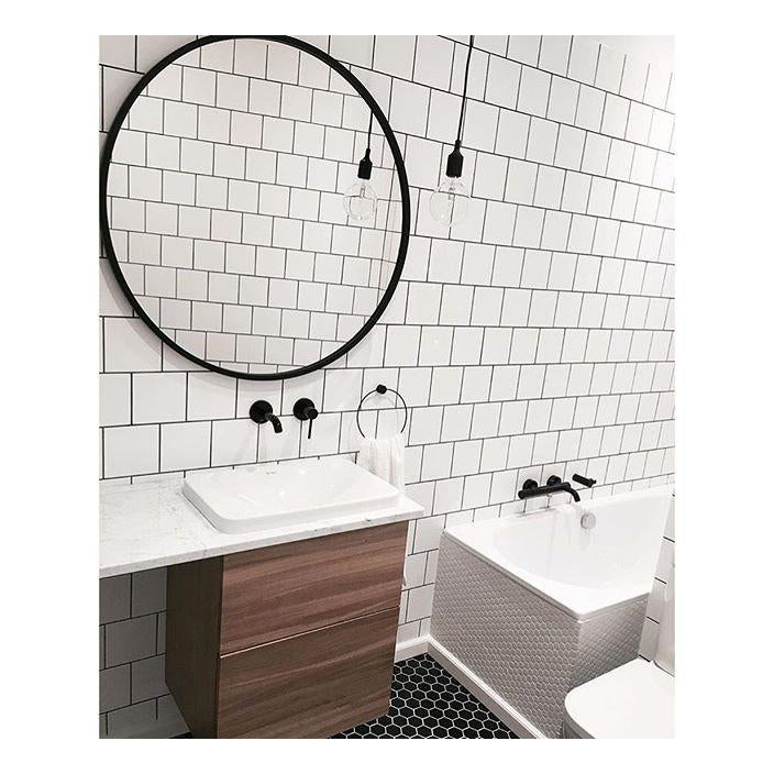 Umbra Hub round mirror in black above a vanity in a white subway tiled bathroom