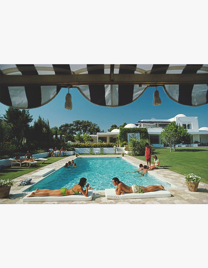 A group of people relaxing in a pool under a Poolside with Slim Aarons awning.