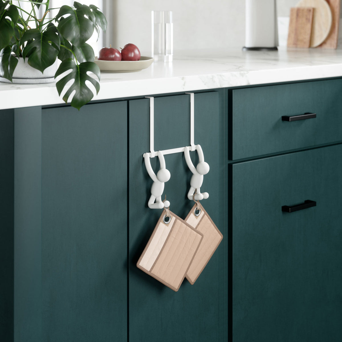 Two Umbra Buddy over-the-door hooks in white on a green kitchen cabinet