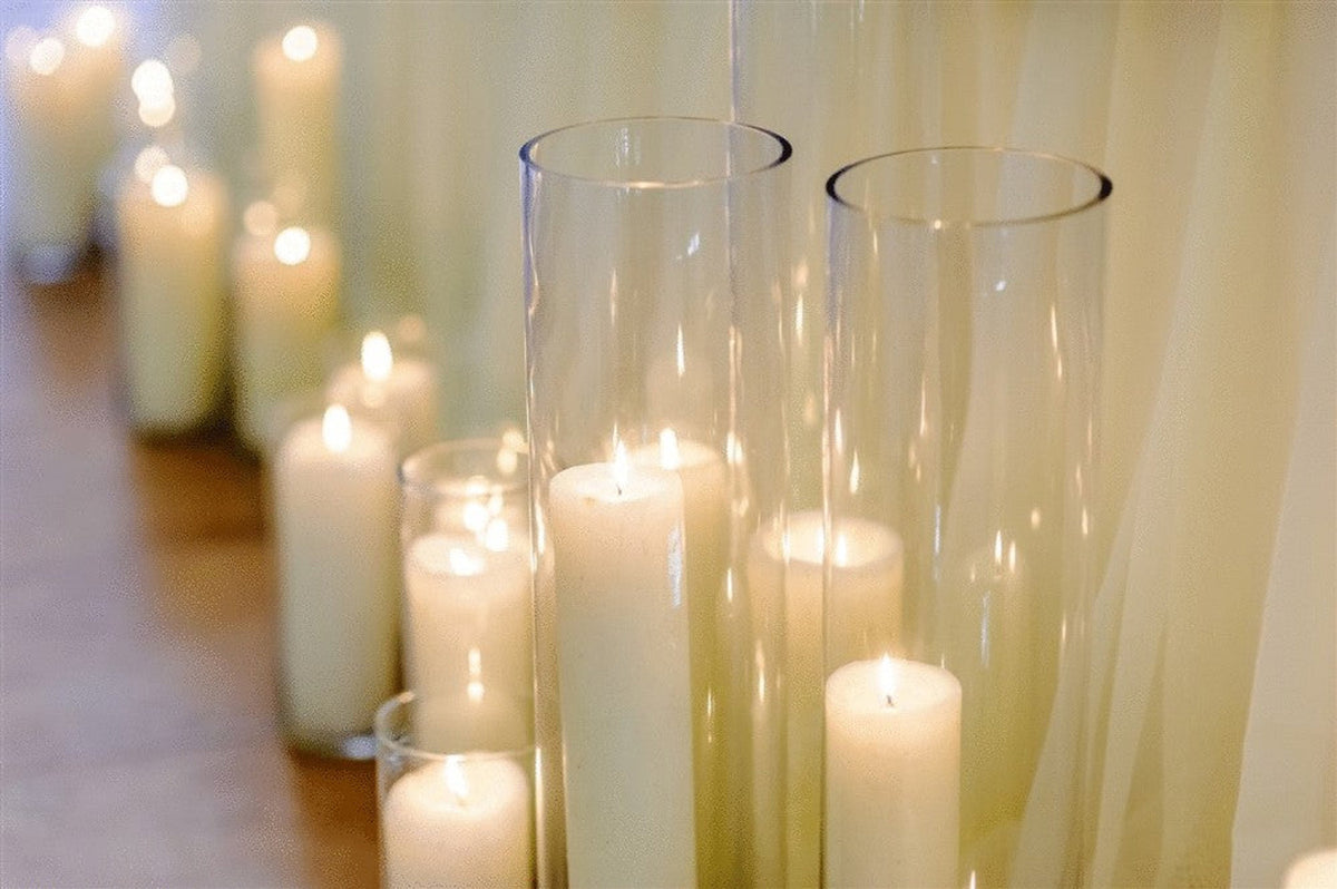 Clear glass cylinder vases holding lit pillar candles among a row of candles
