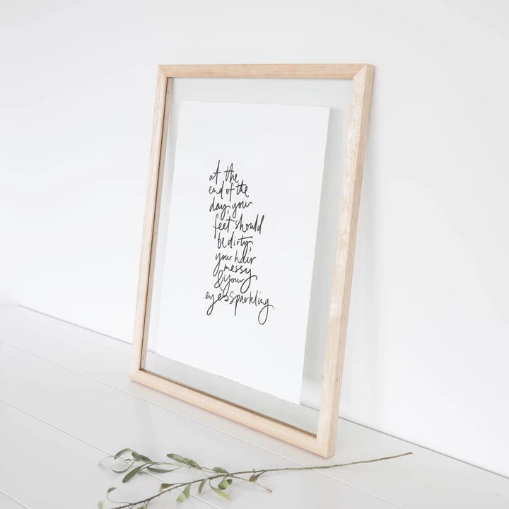 Eyes Sparkling print in a pale timber frame leaning beside a green sprig