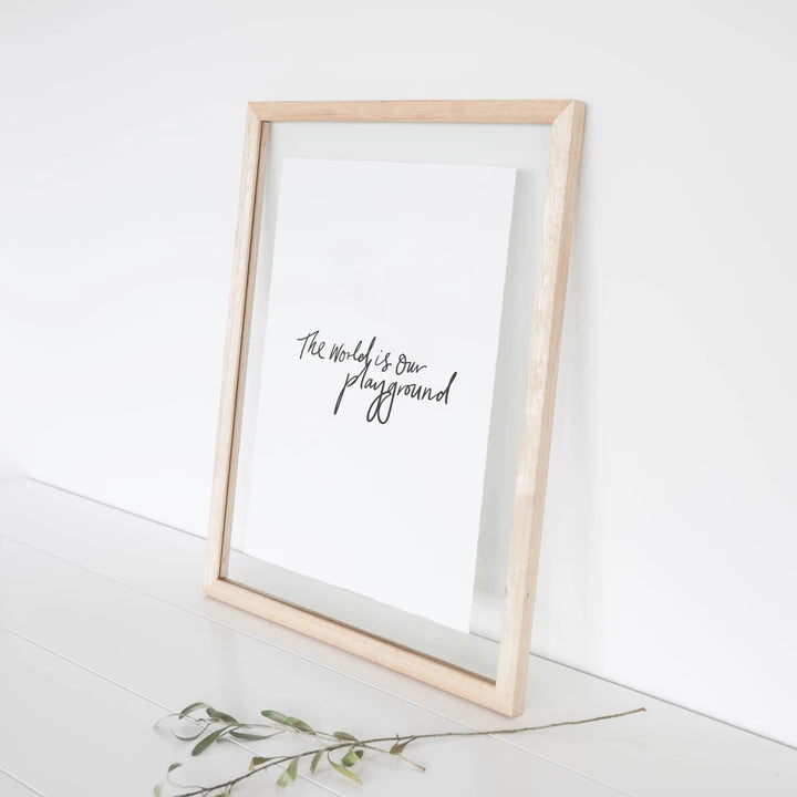 Framed World is Our Playground print leaning on a white wall with a sprig of greenery