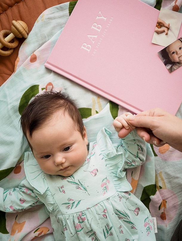 A baby shower gift featuring a baby laying on a pink blanket with a Write To Me Baby Journal.
