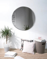 A versatile Hub Mirror - Bevy 36" - Smoke from the Umbra range hangs on a white wall, complemented by the presence of a potted plant.