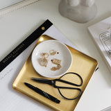 A Papier HQ brass tray on a desk with a pen and a notebook.