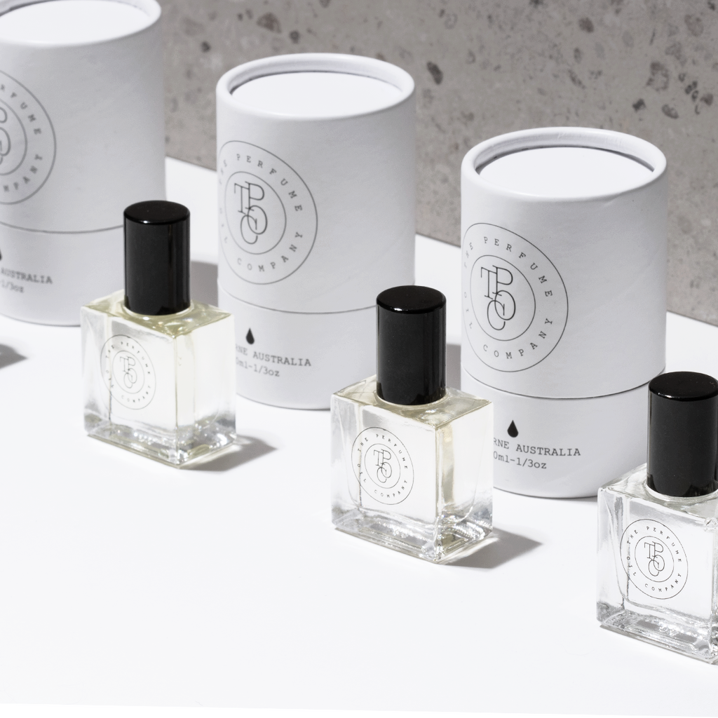 Perfume oil bottles beside white cylindrical gift tubes in grey light