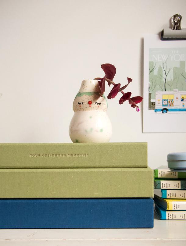 Two sage linen Childhood journals stacked on a blue journal beside a small ceramic vase and kids' books