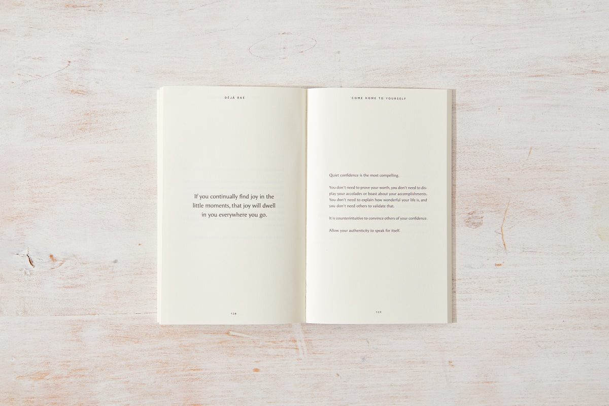 A "Come Home to Yourself | Déjà Rae" design and lifestyle book placed on a wooden surface, by Thought Catalog.