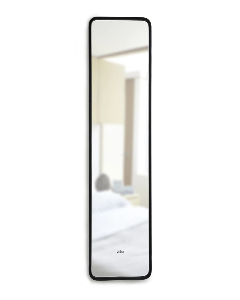 A full-length Umbra mirror, the HUB LEANING MIRROR - BLACK, with a bed placed in front of it.