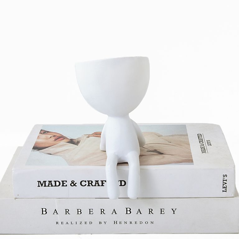 White Egg Head shelf planter with dangling legs, perched on the edge of a stack of books
