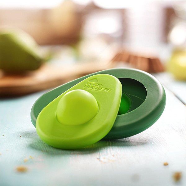 A fresh green SET OF 2 - AVO SAVERS sits on a wooden table. (Brand Name: Food Huggers)