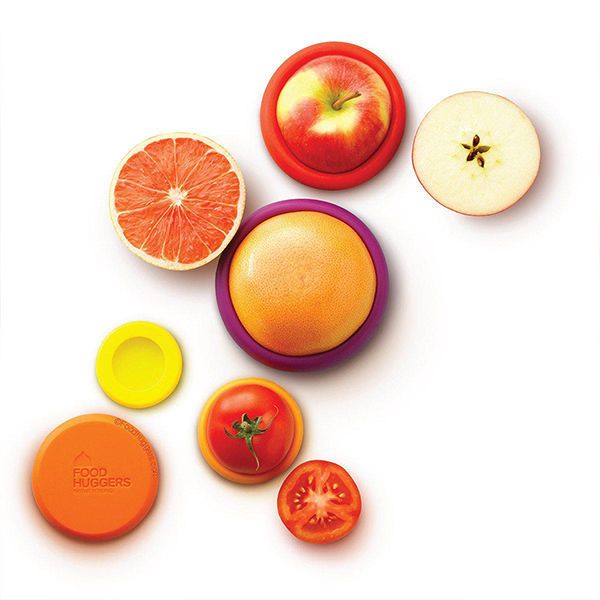 Cut orange, apple and tomato each sealed with a coloured silicone Food Hugger, seen from above