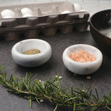 Two Dishy White Marble Spice Bowls with salt and rosemary next to an egg.