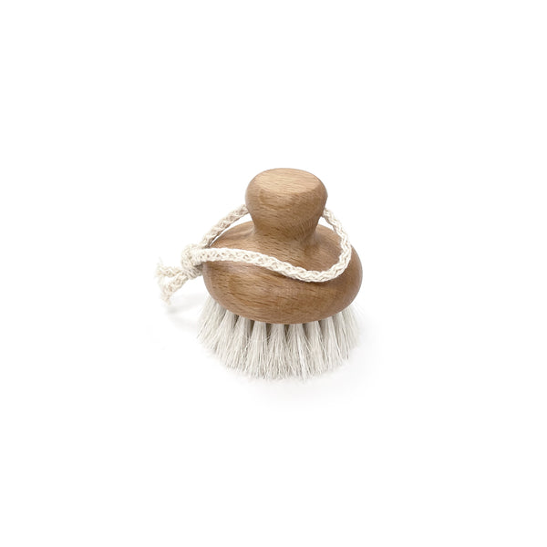 A Florence FACE BRUSH GOAT, a wooden brush with soft goat hair bristles, ideal for gentle exfoliation and massaging the skin. The brush features a convenient rope handle for easy handling. The clean white background highlights