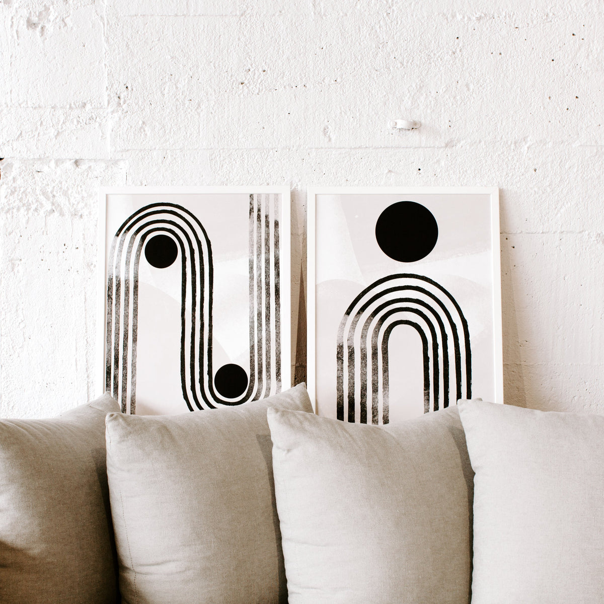Curve Line prints leaning on a white brick wall behind a linen sofa