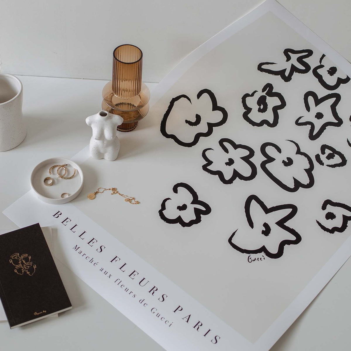 Unframed Fleurs Natural prints on a table beside a glass candle and a black book
