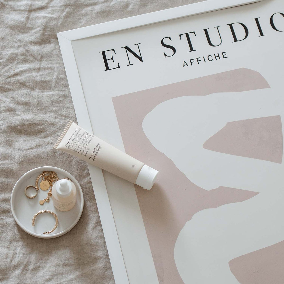 En Studio print lying on linen beside a small dish and a tube