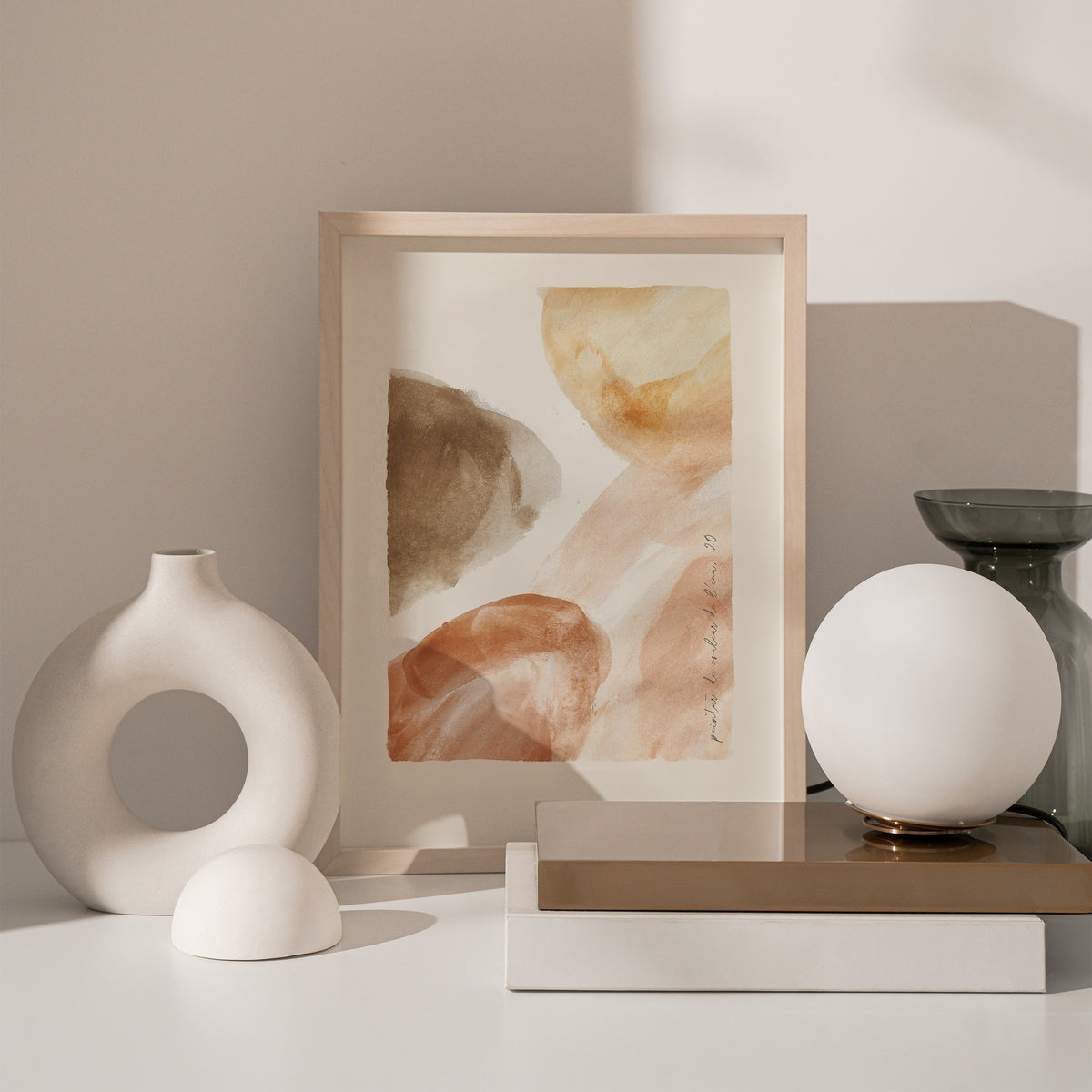 Rust Watercolour print in a natural frame leaning on books beside a white ring vase and a globe lamp