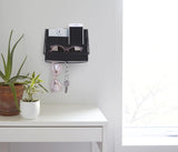 A desk with a plant in an Umbra BOLO PLANTER - White and a cell phone hanging on the wall as part of the wall decor.