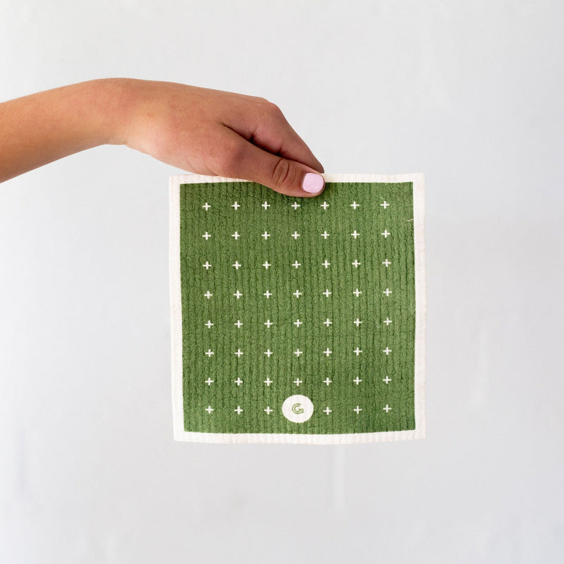 A hand holding a Good Change ECO CLOTH - MEDIUM (3-PACK) cloth towel with green polka dot modern designs.