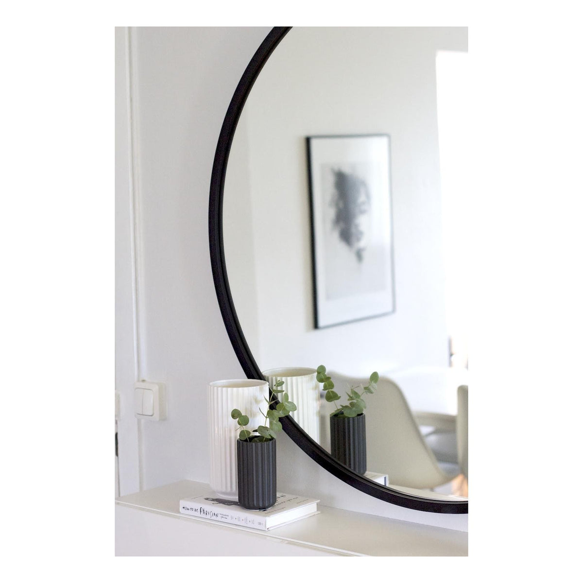 Umbra Hub round mirror in black leaning against a wall beside a framed print