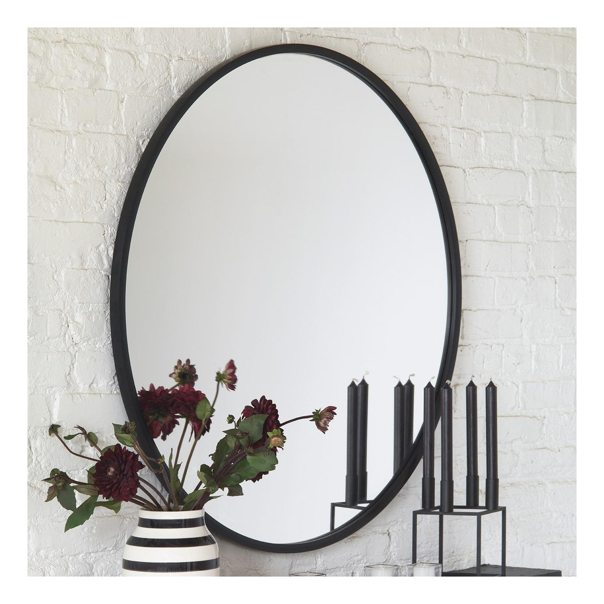 Umbra Hub 94cm round mirror in black on white brick, with a vase and candlesticks
