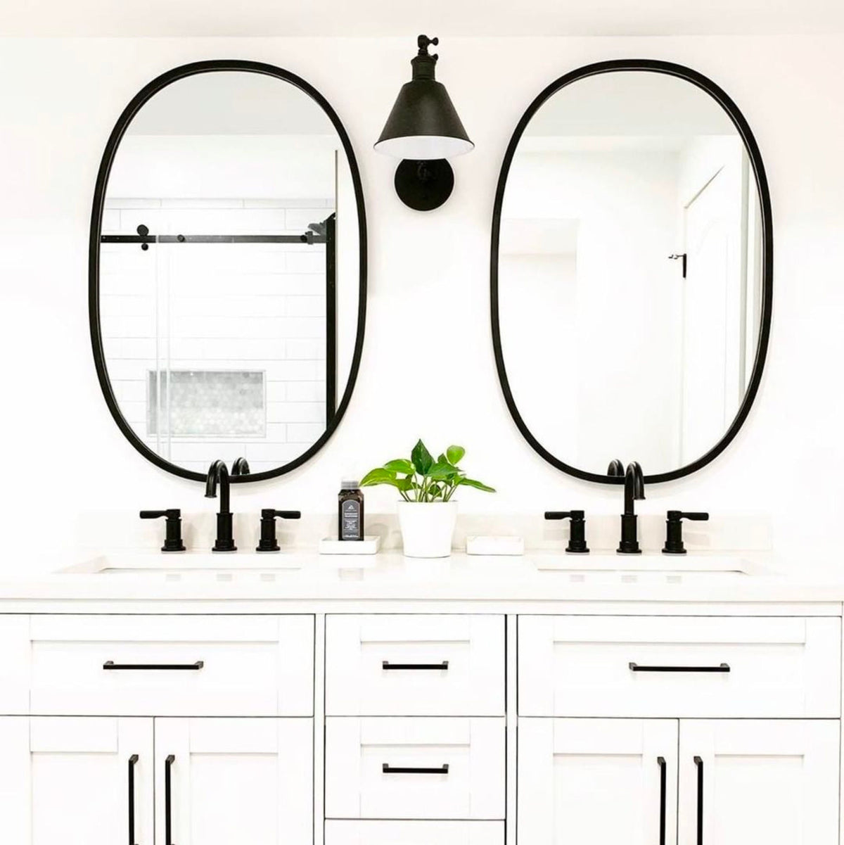 A white bathroom featuring two Umbra Hub Mirror Oval - Black with a rubber rim.