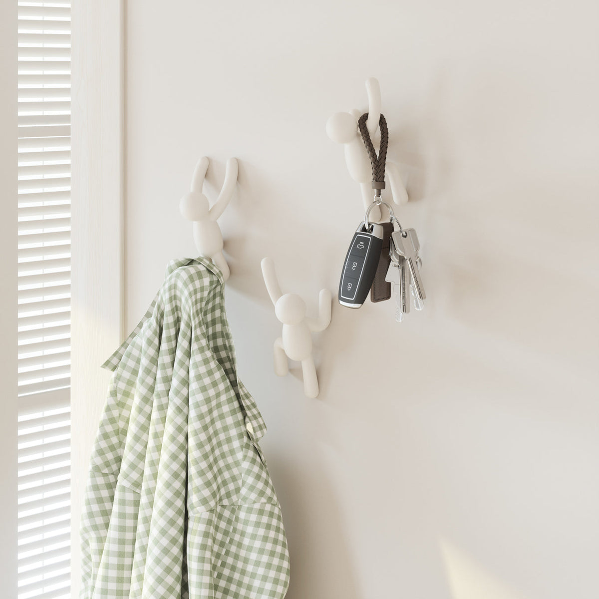 Umbra Buddy hooks in white on a wall holding keys and a green gingham towel