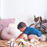 A young boy playing with the Rainbows & Stars Printed Play Pouch by Play Pouch on a blanket in a living room.