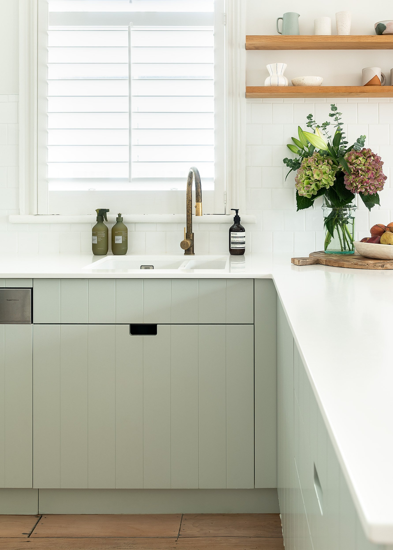 A white kitchen with green cabinets and a window featuring Our Spaces - Contemporary New Zealand Interiors by Books.