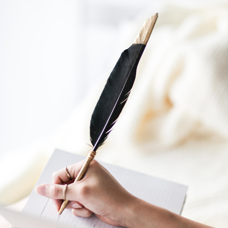 A woman's hand writing in a notebook with the AXEL & ASH Black Feather Pen, capturing the elegance of traditional writing instruments.