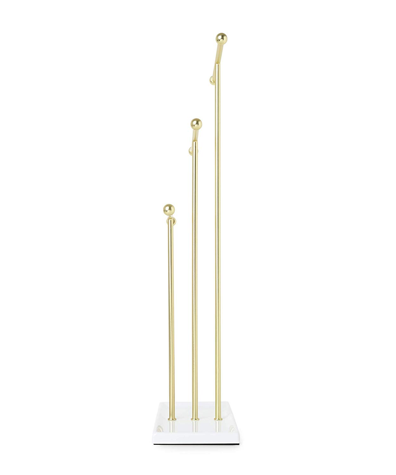 A tangle-free TRIGEM JEWELRY STAND - BRASS featuring three brass rods on a white stand, perfect as a necklace holder. (Brand: Umbra)