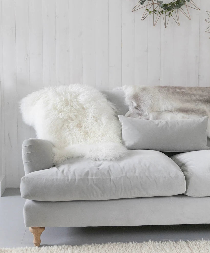 White Tibetan lamb fur draped over the arm and seat of a pale grey sofa