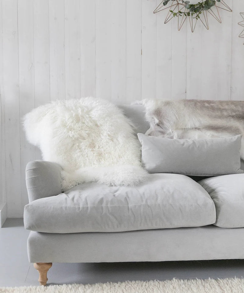A luxury piece - a grey sofa adorned with a Flux Home Tibetan Lamb Fur Double Rug in front of it.