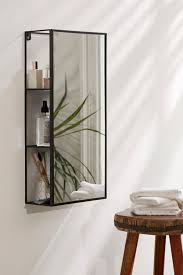 Umbra Cubiko mirror and storage unit in black holding bathroom bottles beside a stool