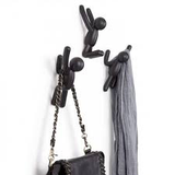 A set of 3 Umbra Buddy Hooks Black serving as a wall décor, with a purse hanging on them.