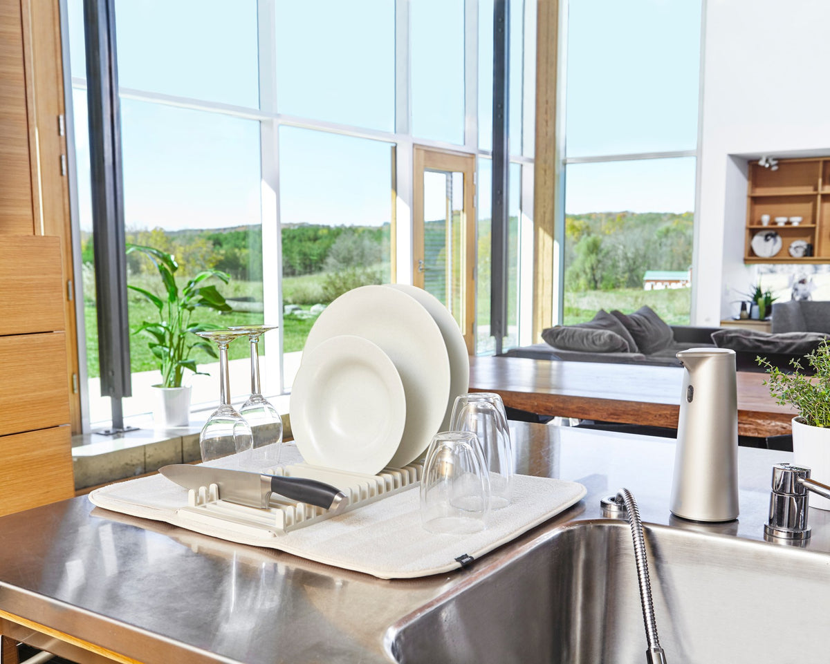 A stainless steel sink with an Umbra Udry Drying Mat Mini in a kitchen.