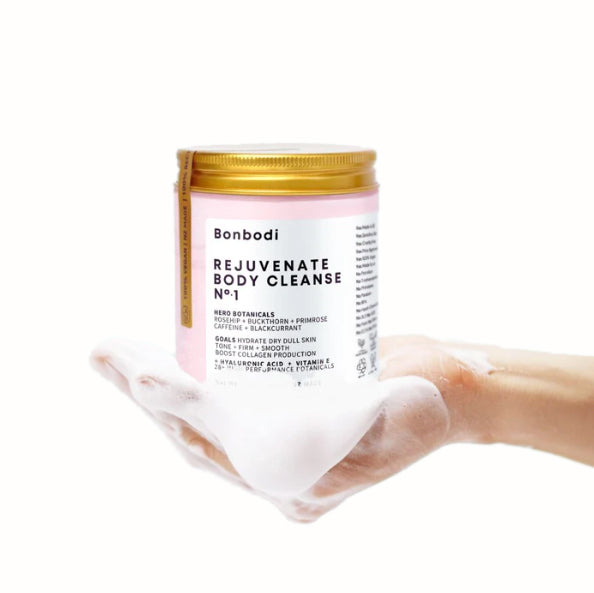 A hand holding a pink jar of Bonbodi's REJUVINATING BODY CLEANSE - HYDRATE + BOOST COLLAGEN botanical body butter that nourishes the skin with hydrating properties, working to boost collagen and elastin for a hydrated and plump appearance.