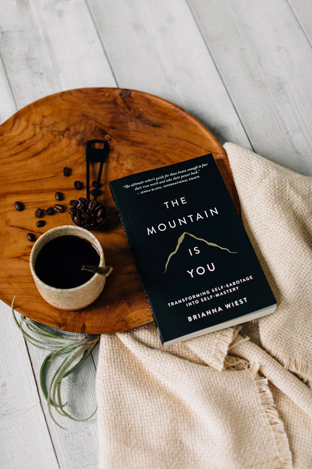 The Mountain Is You by Brianna Wiest resting on a wooden tray beside a cup of coffee