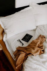 A bed with pillows, blankets and a book - The Mountain Is You by Brianna Wiest from Thought Catalog.
