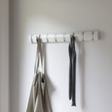 A Flip 8 Hook White wall mounted coat rack from the Umbra range, featuring retractable hooks, with a bag hanging on it.