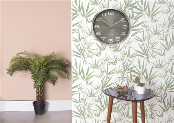 Maxie wall clock on botanical wallpaper above a side table, beside a potted palm on a pink wall
