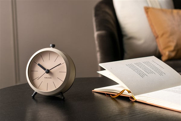 Warm grey Button alarm clock on a dark bedside table beside an open book