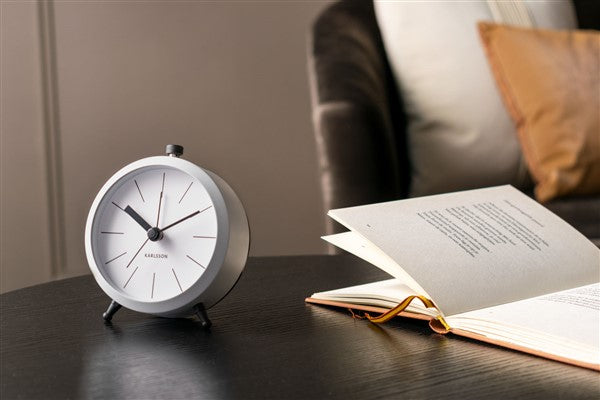 White Button alarm clock on a dark bedside table beside an open book