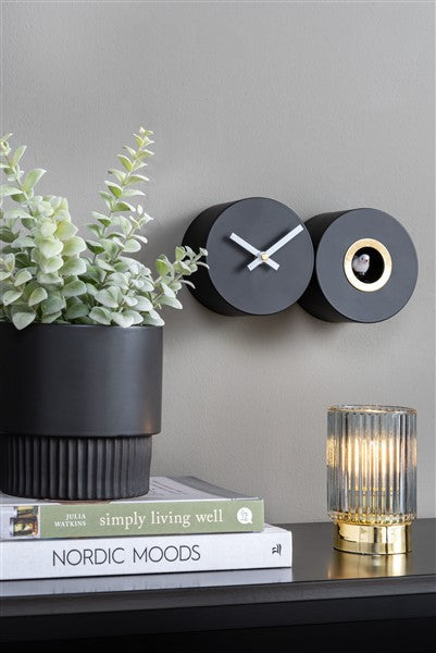 A Duo Cuckoo wall clock by Karlsson on a shelf next to a potted plant.