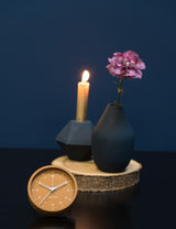 A small foldable Karlsson Tinge Alarm Clock placed next to a vase and a candle.