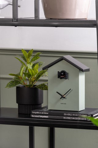 A Cuckoo Traditional - Various Options wall clock placed on a shelf near a potted plant.