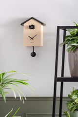 A Cuckoo Traditional - Various Options wall clock by Karlsson hanging on a wall next to a potted plant.