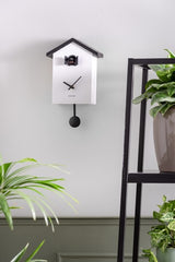 A Cuckoo Traditional - Various Options wall clock hanging on a ladder next to a potted plant.